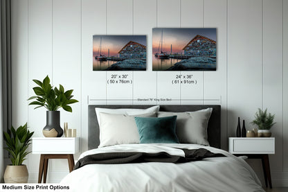 a bedroom with a bed, nightstands, and potted plants. There are two framed prints hanging on the wall above the bed, depicting a seascape with a building and boats. The prints are of different sizes, ranging from 24" x 36" to 50" x 70" (71" x 91").