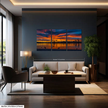 A modern living room with a large wall art depicting a sunset over a body of water. The room has a white sofa, a wooden coffee table, and a large window that allows natural light to fill the space.
