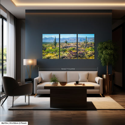 A modern living room with a large wall-mounted painting depicting a desert landscape with cacti and mountains. The room has a gray sofa, a wooden coffee table, and a large window overlooking the desert.