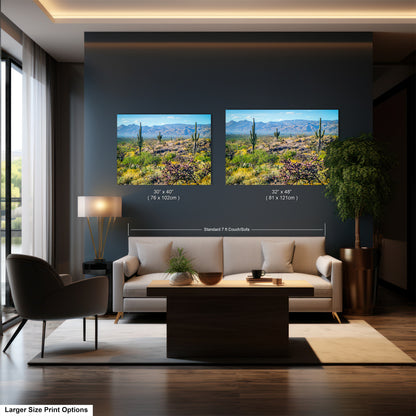 a modern living room with a large sofa, a coffee table, and a potted plant. Two framed landscape paintings are displayed on the wall above the sofa, depicting a desert scene with mountains in the background.