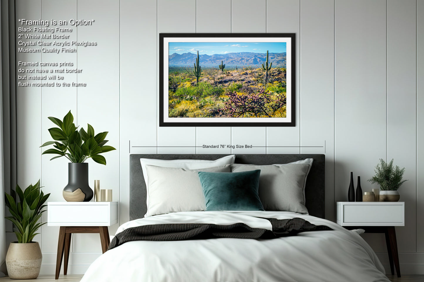 a bedroom with a large framed picture of a desert landscape hanging on the wall above a bed. The bed has a black headboard and white bedding. The room also includes a nightstand on each side of the bed, with a plant on each nightstand. The walls are painted white, and there is a window in the room.