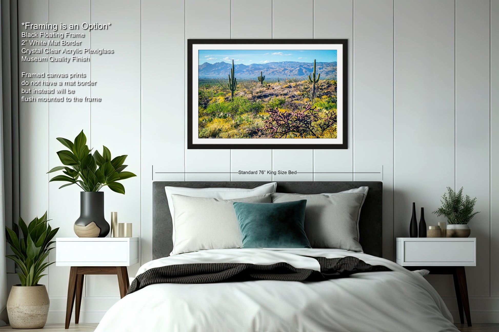 a bedroom with a large framed picture of a desert landscape hanging on the wall above a bed. The bed has a black headboard and white bedding. The room also includes a nightstand on each side of the bed, with a plant on each nightstand. The walls are painted white, and there is a window in the room.