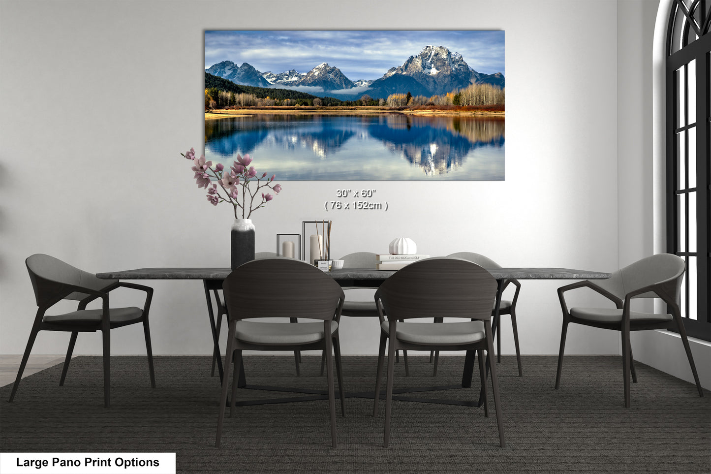 A large pano print depicting a serene mountain landscape with a lake and snow-capped peaks, hanging on a wall above a dining table with chairs.