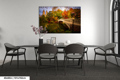 a large painting of a scenic landscape with a bridge and trees, hanging on a wall above a dining table with chairs.