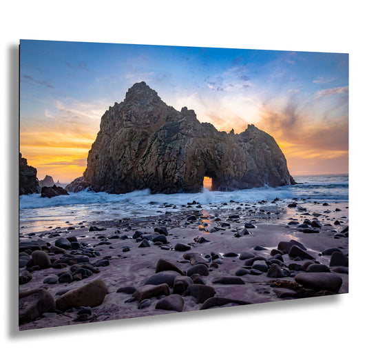 a rock formation on a beach with a sunset in the background