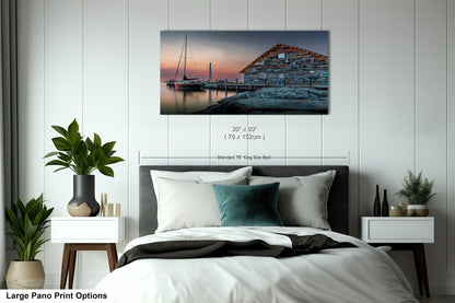 a modern office or conference room setting with a large wooden table surrounded by chairs. There are two framed prints displayed on the wall above the table, depicting a seascape with a building and a sailboat. The prints are of similar size and style, suggesting they are part of a medium pano print option.