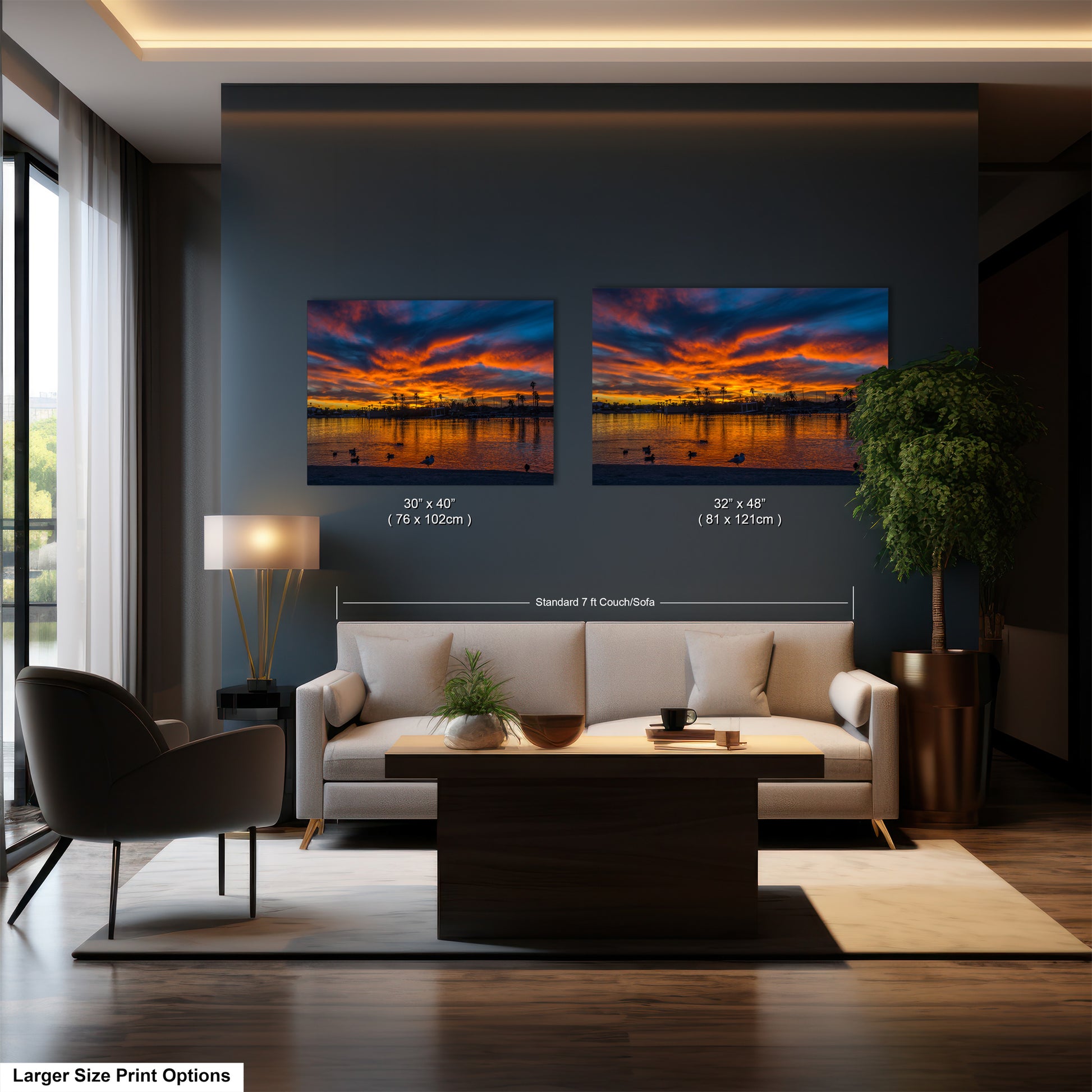 The image is a modern living room with a large sofa, a coffee table, and a lamp. Two framed landscape paintings are hanging on the wall above the sofa, depicting a sunset over a body of water.