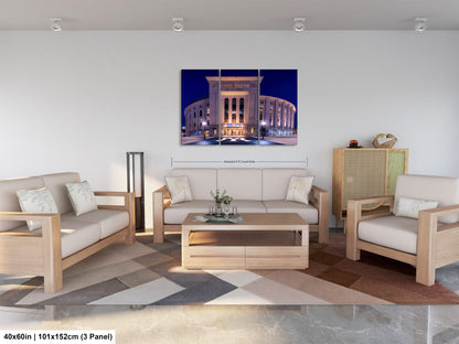 The image is a modern living room with a large, illuminated building in the background. The room is furnished with a sofa, two chairs, and a coffee table. The furniture appears to be made of wood and has a neutral color scheme. The room is well-lit, with natural light coming in from the windows. The overall design and layout of the room create a comfortable and inviting atmosphere.