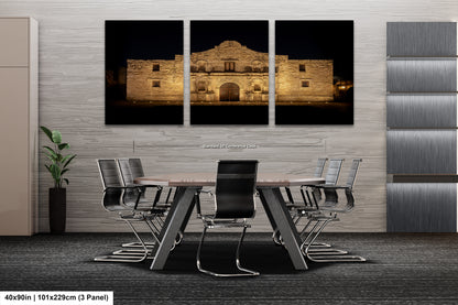 A modern office space with a large, illuminated photograph of the historic Alamo in the background. The photograph is displayed on the wall above a conference table with chairs.