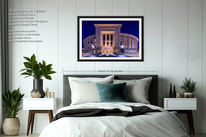 a bedroom with a large framed picture of a building, a bed with a black and white striped comforter, and a nightstand with a plant and a candle.