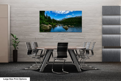 A modern office space with a large wall-mounted painting depicting a scenic lake surrounded by mountains. The painting is framed in a wooden frame and hangs above a wooden table with chairs.