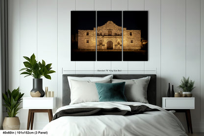 a large, illuminated building at night, with a bed in the foreground and two nightstands on either side.