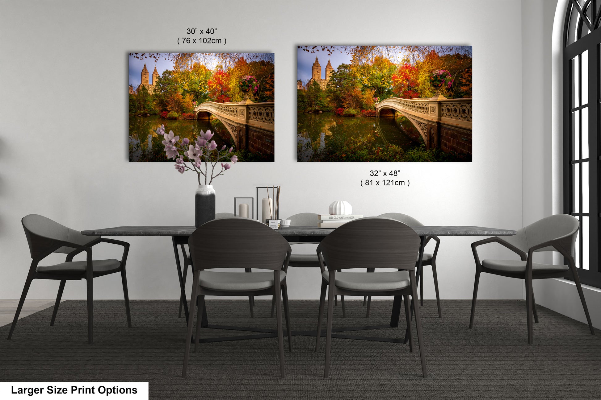 a dining room with a large dining table and six chairs. There are two framed paintings of a scenic bridge hanging on the wall above the table. The paintings are of different sizes, with one being larger than the other. The table is set with a vase of flowers and a few other items, creating a cozy and inviting atmosphere.