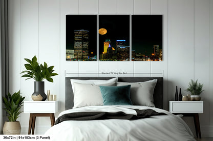 a bed room with a neatly made bed and a night time view of a city