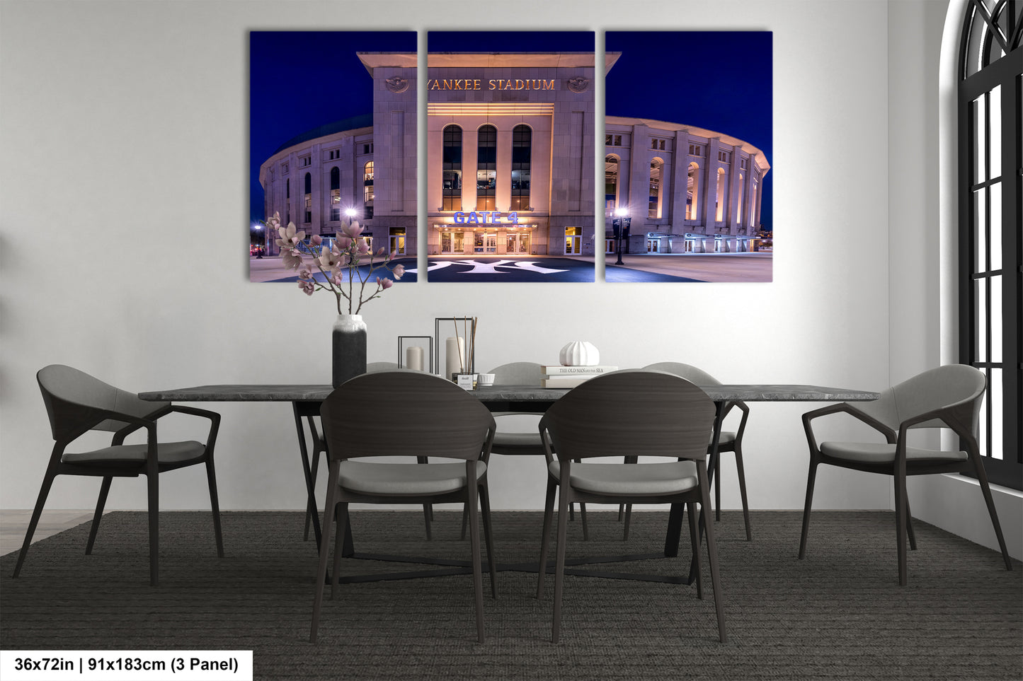 A large, three-panel canvas artwork depicting the exterior of Yankee Stadium at night, with the stadium's name prominently displayed. The artwork is mounted on a wall above a dining table with chairs.