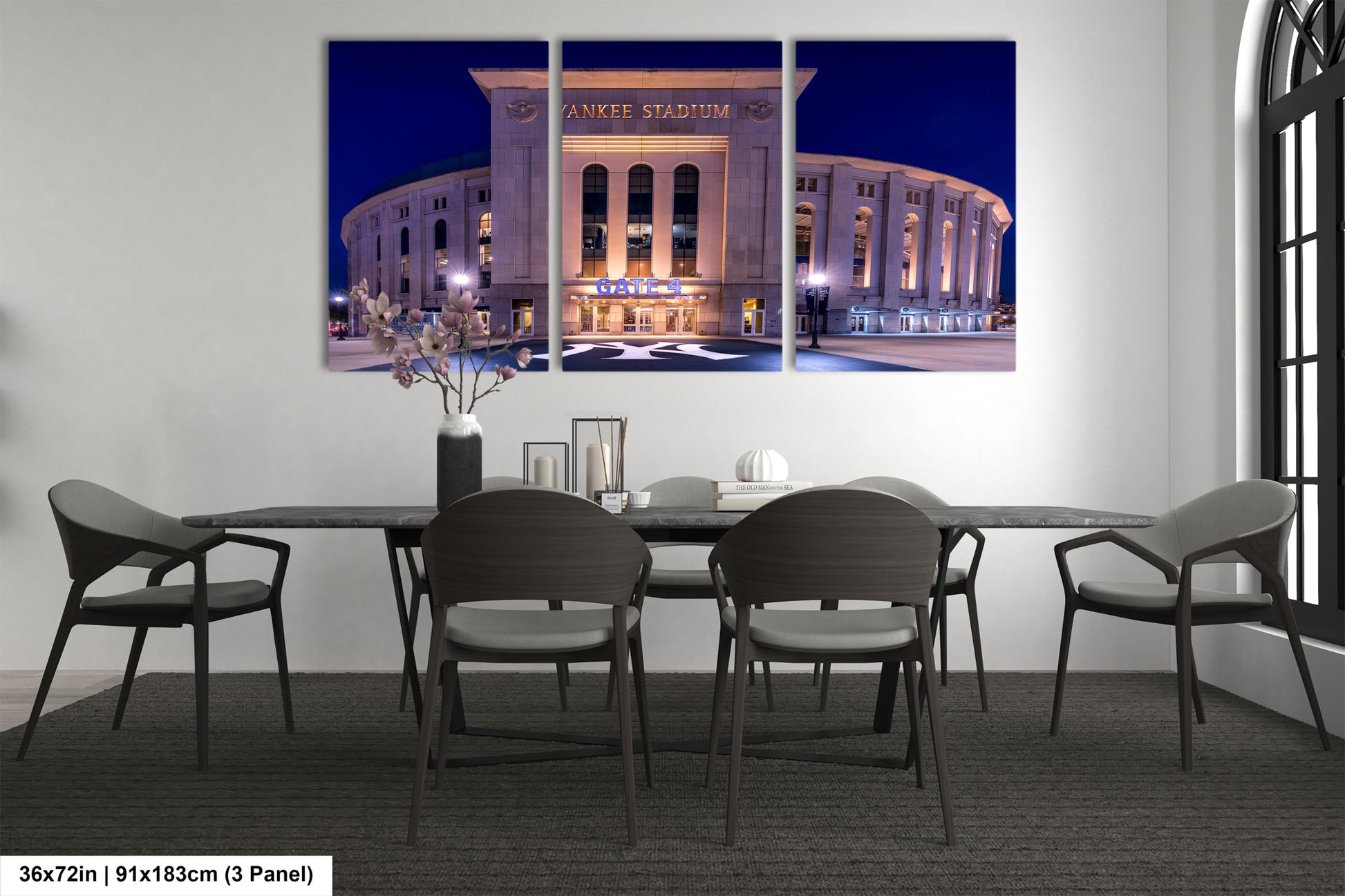 A large, three-panel canvas artwork depicting the exterior of Yankee Stadium at night, with the stadium's name prominently displayed. The artwork is mounted on a wall above a dining table with chairs.
