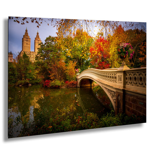 a picturesque scene of a stone bridge spanning a tranquil pond, surrounded by a vibrant display of autumn foliage. The bridge is adorned with flowers, adding a touch of elegance to the scene. In the background, the iconic New York City skyline, including the famous Central Park, can be seen, creating a beautiful contrast between the natural beauty of the park and the architectural marvel of the city.