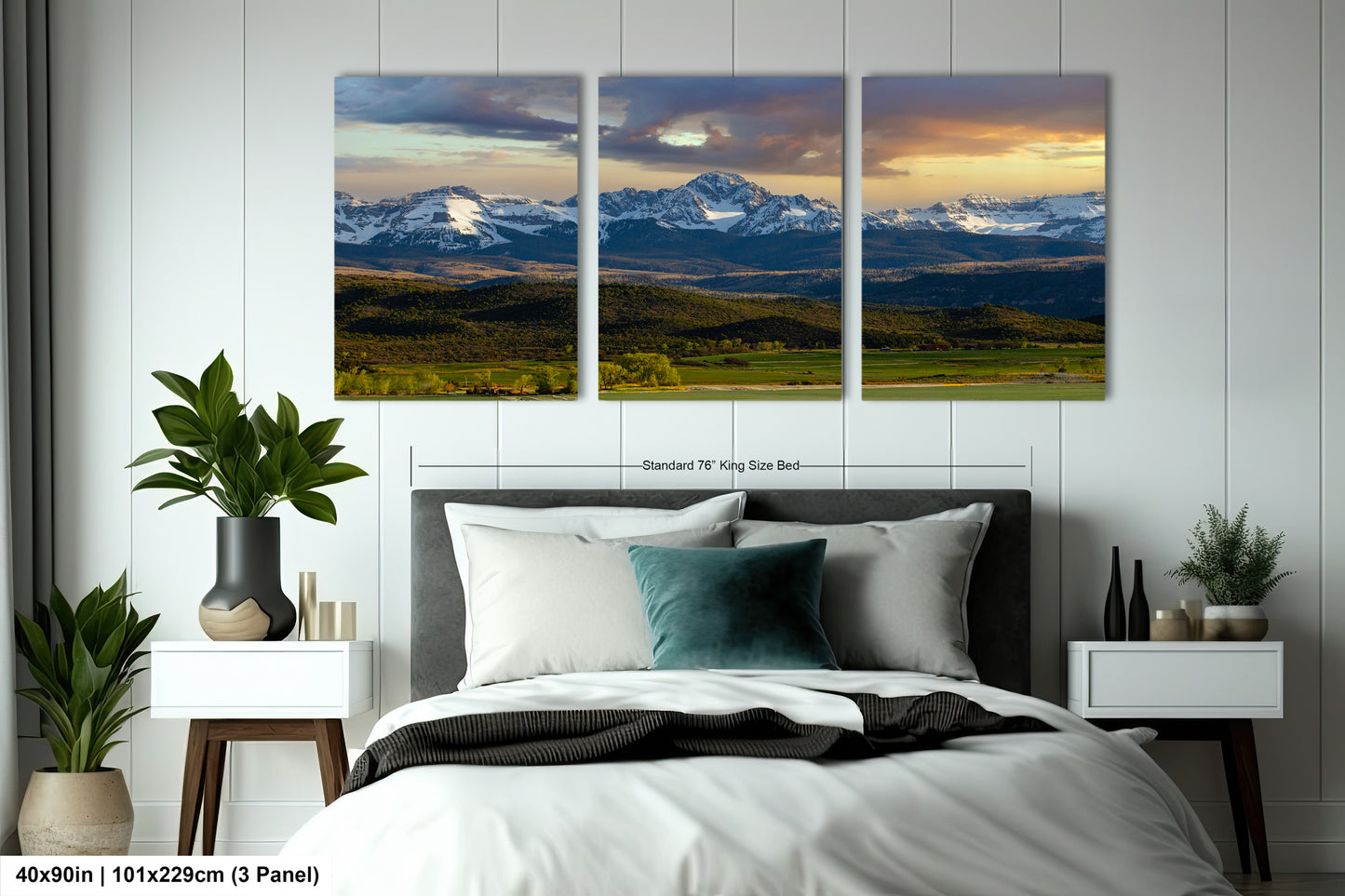 The image is a bedroom with a large, three-panel landscape painting hanging on the wall above the bed. The painting depicts a scenic mountain range with a cloudy sky, creating a serene and picturesque atmosphere.