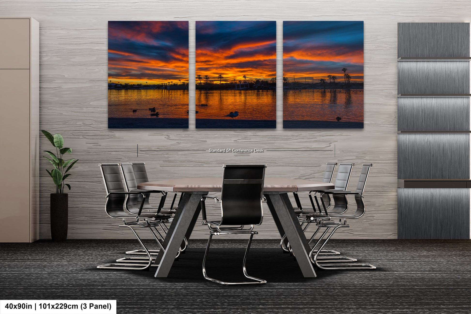 A modern office space with a large, three-panel landscape painting depicting a sunset over a body of water. The painting is mounted on a gray wall above a wooden table surrounded by chairs.