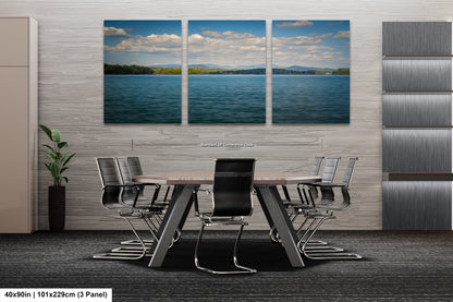 A modern office space with a large wall-mounted painting depicting a serene landscape of a lake and mountains. The painting is divided into three panels, creating a sense of depth and perspective. The office features a wooden table surrounded by black chairs, and a plant in a vase is placed on the floor. The image is described as a collage of multiple images, and the dimensions provided are 40.9in by 101.29cm by 3 panels.