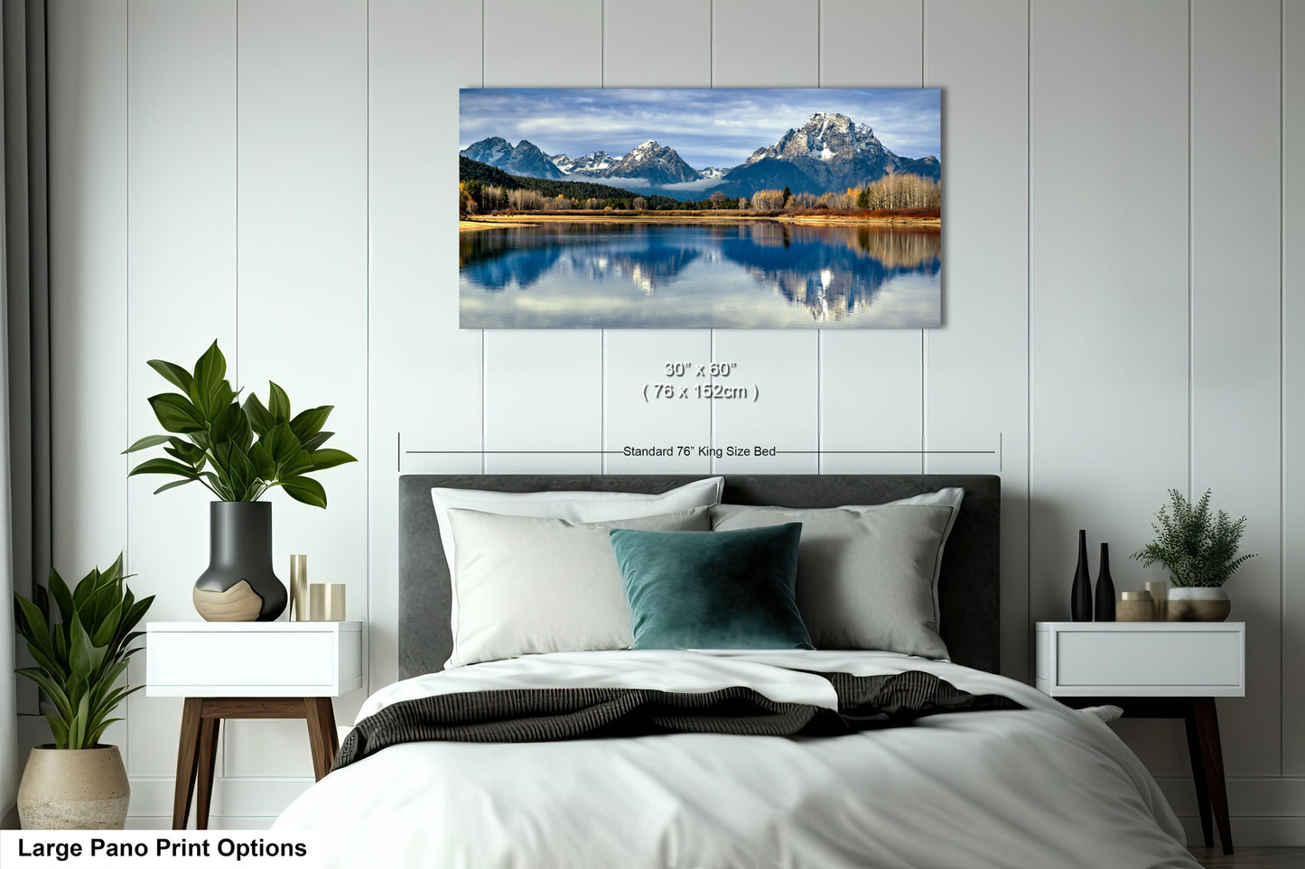 A large pano print depicting a serene mountain landscape with a lake reflecting the sky, hanging on a wall above a bed with white bedding and a green throw pillow.