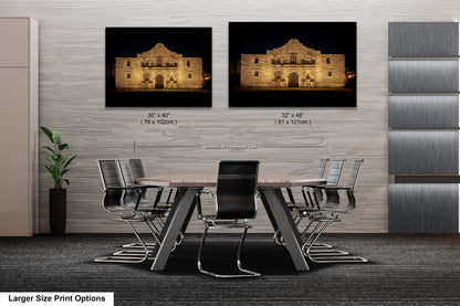 a modern office space with a large wooden table surrounded by black chairs. Two framed photographs of the Alamo in Texas are displayed on the wall above the table.
