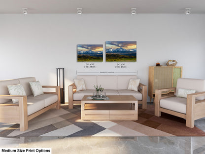 a living room with a sofa, two chairs, and a coffee table. The sofa and chairs are white, and the coffee table is made of wood. There is a rug on the floor, and the walls are painted white. Two framed landscape paintings are hanging on the wall, one depicting a mountain range and the other showing a sunset. The image also includes text that provides information about the medium size print options for the artwork.