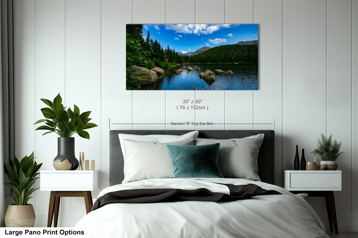 A large pano print depicting a serene landscape with a lake, mountains, and trees is displayed on the wall above a bed with white linens and pillows.