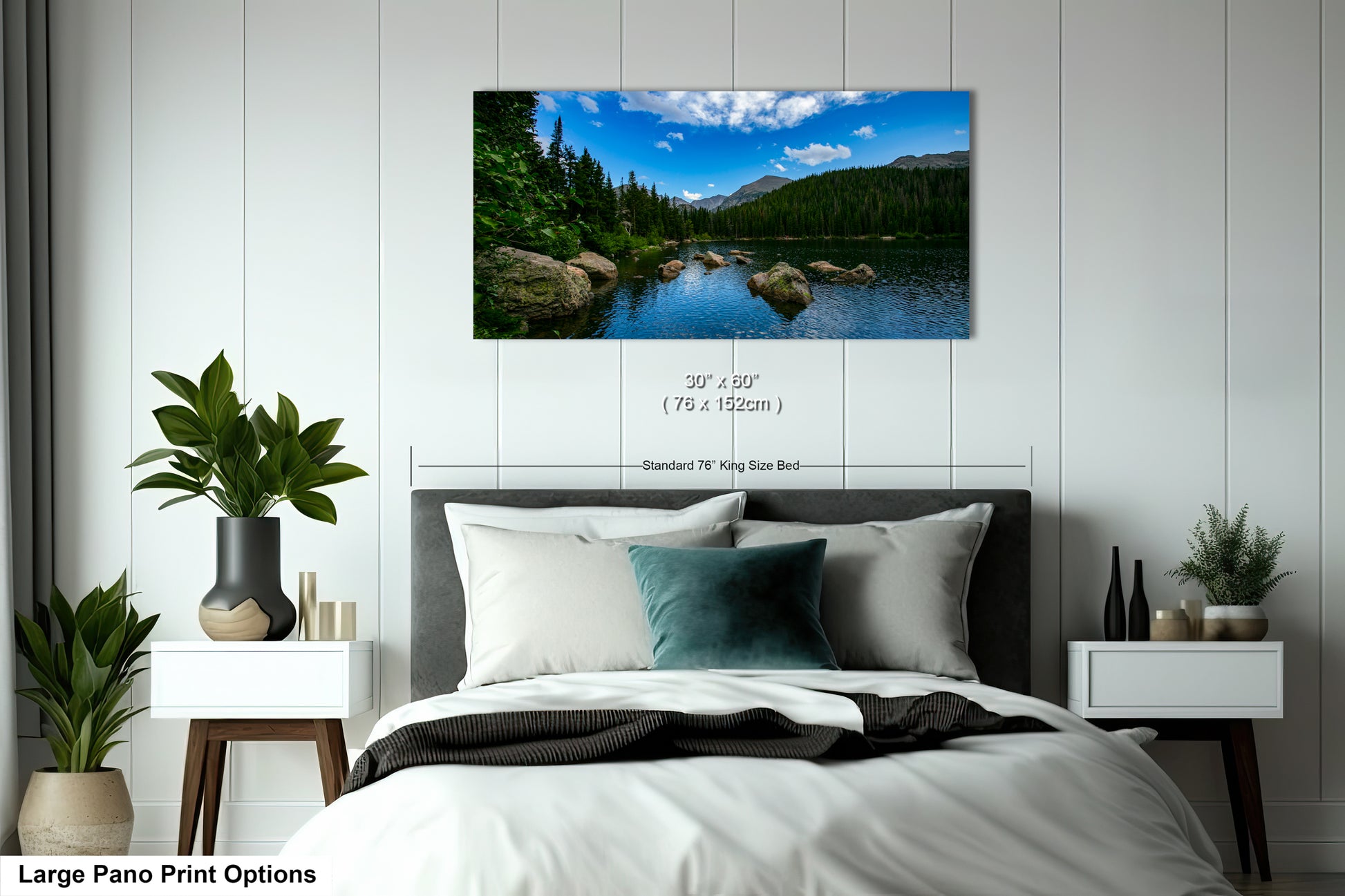 A large pano print depicting a serene landscape with a lake, mountains, and trees is displayed on the wall above a bed with white linens and pillows.