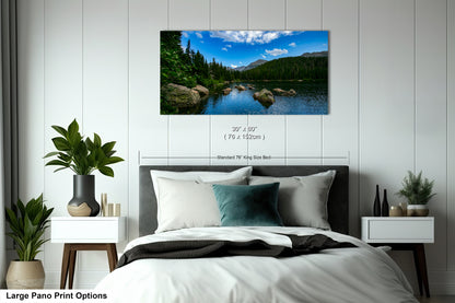 A large pano print depicting a serene landscape with a lake, mountains, and trees is displayed on the wall above a bed with white linens and pillows.