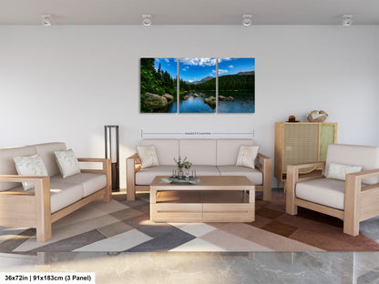 The image is a modern living room with a large, three-panel landscape painting hanging on the wall. The painting depicts a serene mountain lake surrounded by trees and mountains, creating a peaceful and natural atmosphere. The room is furnished with a sofa, two armchairs, and a coffee table, providing a comfortable and inviting space for relaxation and socializing.
