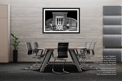 a modern office space with a large black and white photograph of a building on the wall, a wooden table surrounded by black chairs, and a plant in a black vase on the floor.