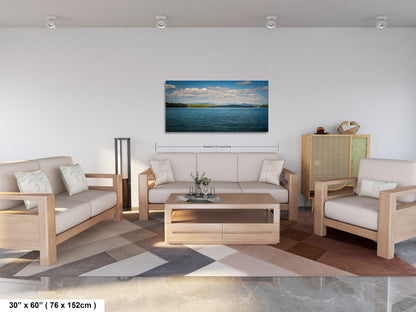 a modern living room with a large, rectangular, wooden coffee table in the center, surrounded by two white couches and a matching chair. Above the coffee table, there is a large, framed picture of a serene body of water with a blue sky and clouds. The room has a clean, minimalist design with white walls and a gray and brown patterned rug on the floor.