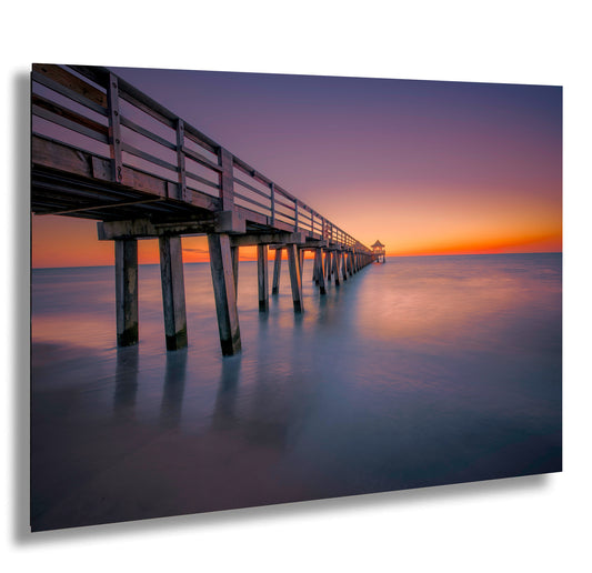 a long pier stretches out into the ocean at sunset