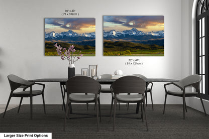 a dining room with a large dining table surrounded by six chairs. Two large landscape paintings are displayed on the wall above the table, depicting a scenic mountain landscape with a colorful sky.
