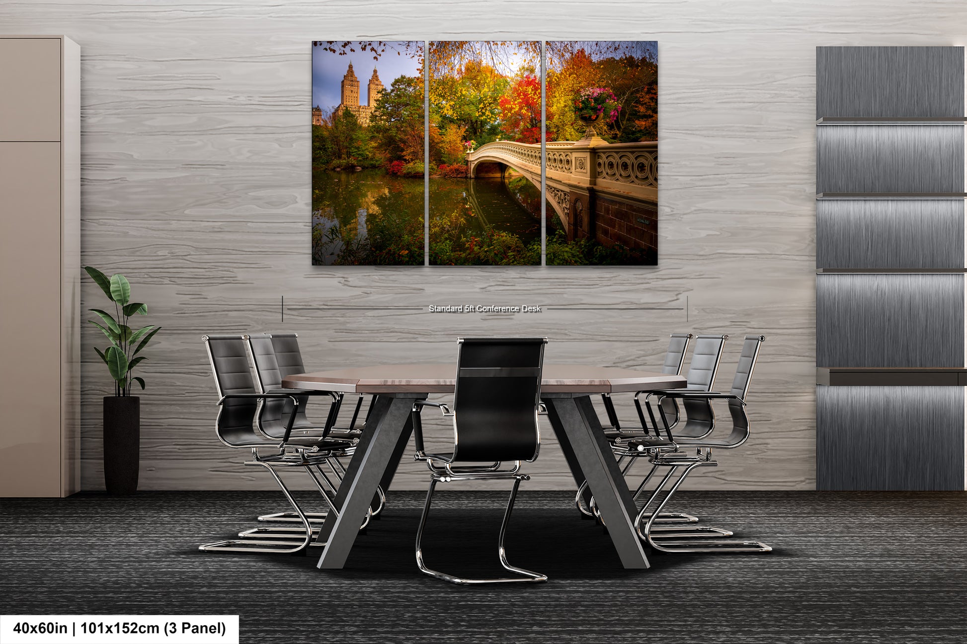 The image is a modern office space with a large, multi-paneled wall art depicting a scenic view of Central Park in New York City. The art features a bridge and trees in autumn colors, creating a serene and natural atmosphere. The office has a sleek, contemporary design with a gray and white color scheme, and the table and chairs are arranged for a meeting or presentation.