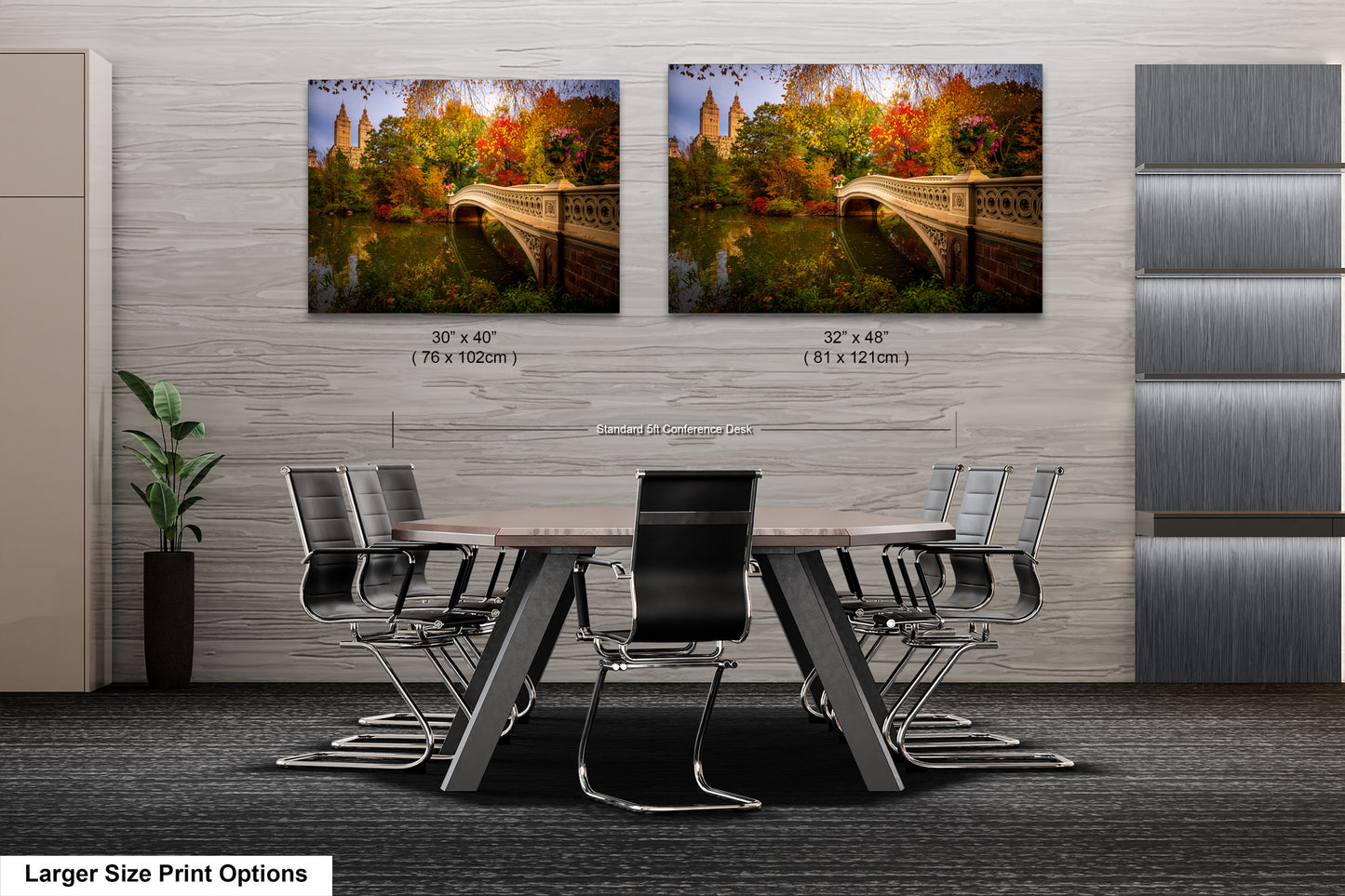 a modern office space with a large wooden table surrounded by black chairs. Two framed prints of a scenic bridge and autumn foliage are displayed on the wall above the table.