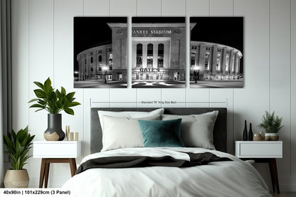 A bedroom with a large wall-mounted print of the Yankee Stadium in New York City at night. The print features the stadium's exterior and surrounding area, with the words "Yankee Stadium" prominently displayed. The print is framed by a black border, and the dimensions are provided as "40in (101.29cm) (3 panel)".
