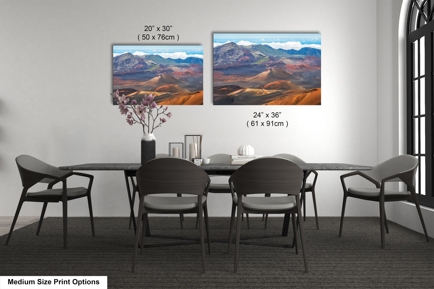 a modern dining room with a large black table surrounded by six chairs. Two large landscape paintings are displayed on the wall above the table, depicting a mountainous desert scene. The paintings are framed in a medium size, and the dimensions are provided in inches.