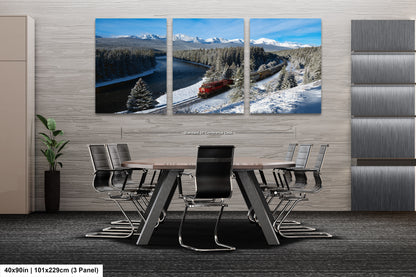 A modern office space with a large, three-panel landscape painting depicting a snowy mountain scene with a train passing through it. The painting is mounted on the wall above a wooden table surrounded by chairs.