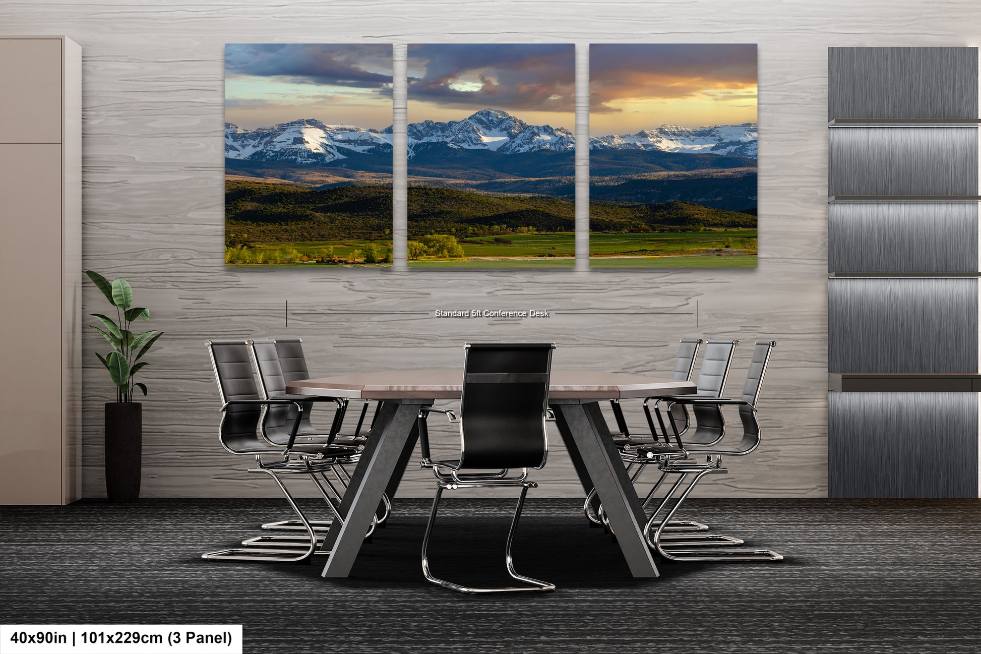 A modern office space with a large, three-panel landscape painting depicting a scenic mountain range and valley. The painting is mounted on the wall above a wooden table surrounded by chairs.