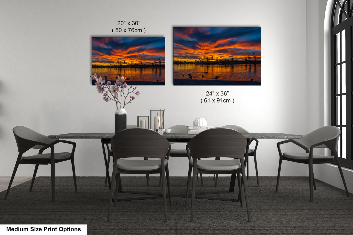 a modern dining room with a large dining table and six chairs. Two large paintings of a sunset are displayed on the wall above the table, creating a serene and artistic atmosphere.