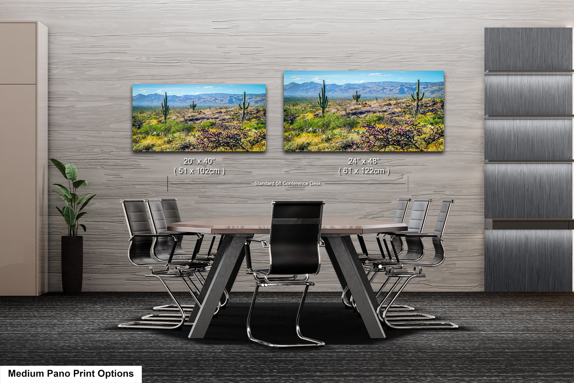 a modern office or conference room setting with a large wooden table surrounded by black chairs. Two framed landscape paintings are displayed on the wall above the table, depicting a desert scene with mountains in the background.