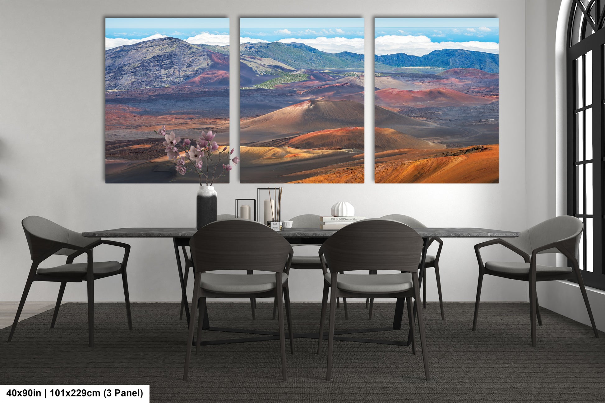a large, panoramic landscape painting depicting a desert scene with mountains in the background. The painting is divided into three panels, with the top and bottom panels showing a desert landscape and the middle panel showing a mountain range. The painting is hung on a wall above a dining table with chairs arranged around it.