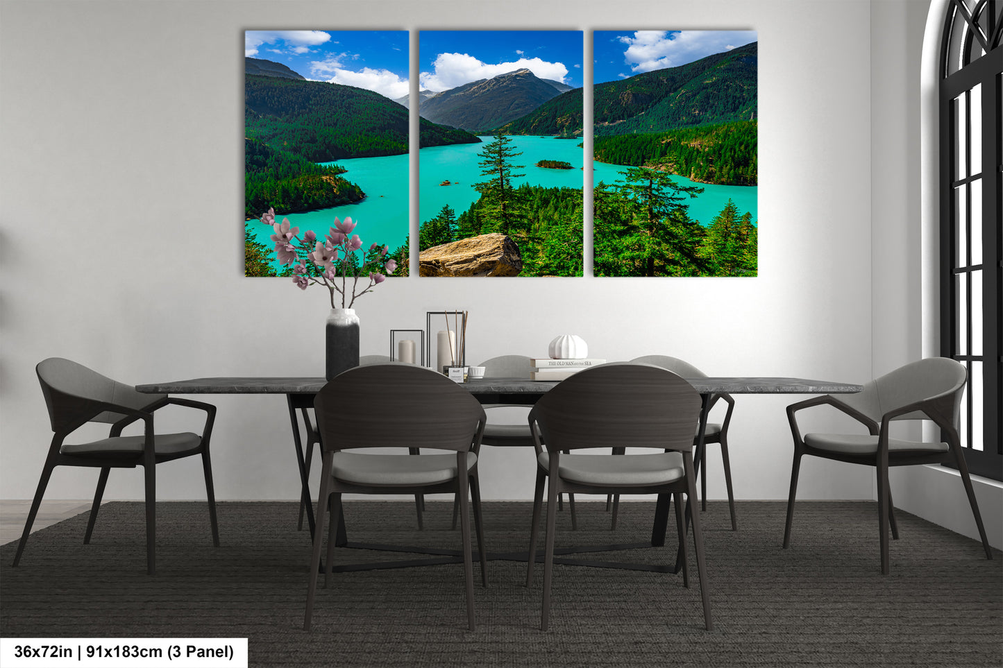 a modern dining room with a large, three-panel landscape painting depicting a scenic mountain lake surrounded by lush forests. The painting is hung on the wall above a black dining table with six chairs. The room has a minimalist and contemporary design, with a vase of flowers and a few decorative items on the table.