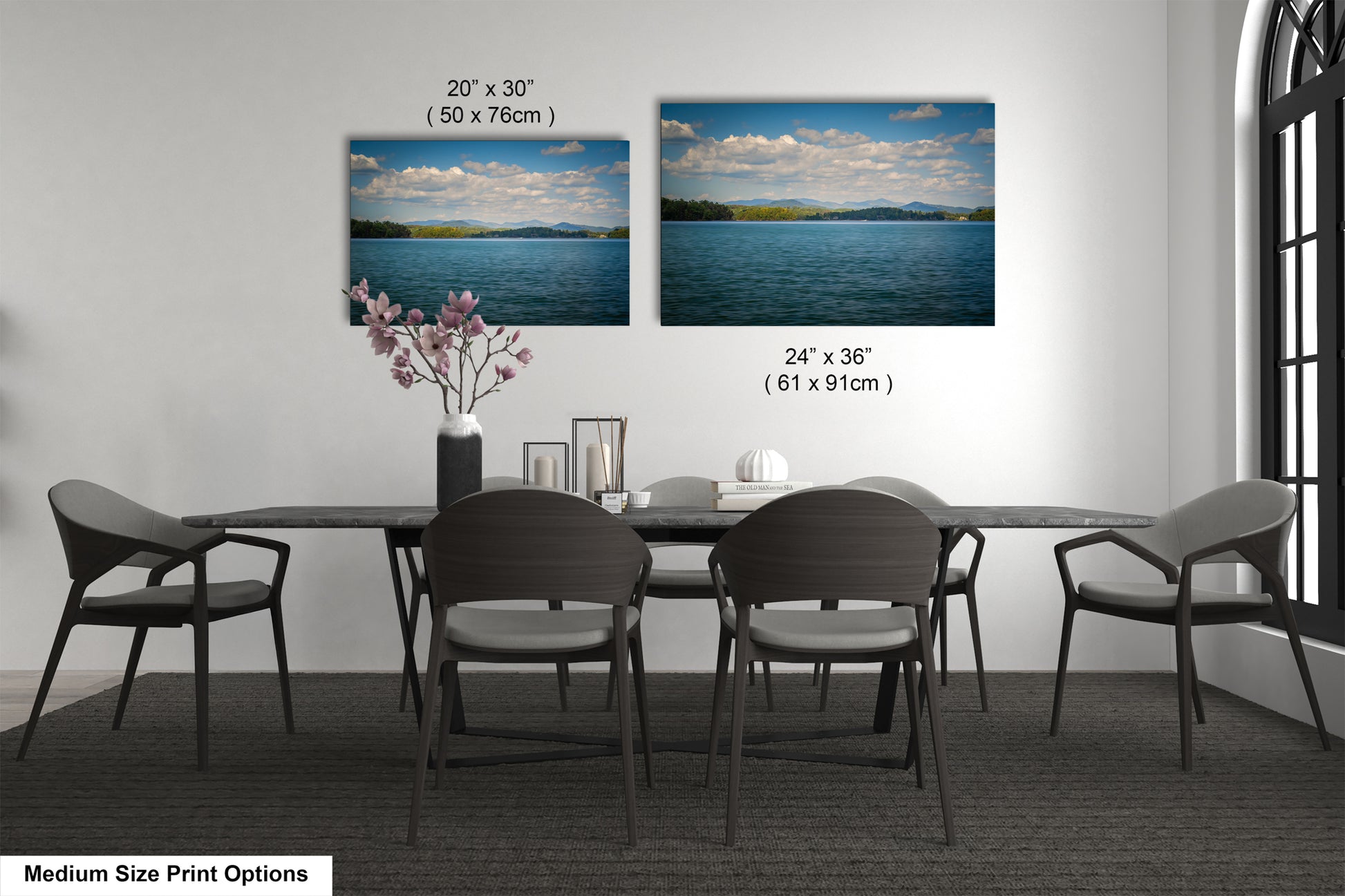 a dining room with a large dining table surrounded by six chairs. There are two framed landscape paintings hanging on the wall above the table, depicting a serene lake scene with mountains in the background. The paintings are of medium size, with dimensions of 20' x 30' (50 x 76') and 24' x 36' (61 x 91') respectively.