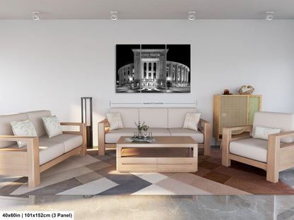 a modern living room with a large black and white photograph of a stadium or arena on the wall. The room is furnished with a sofa, two chairs, and a coffee table. The photograph is framed and hangs above the furniture, creating a focal point in the space.