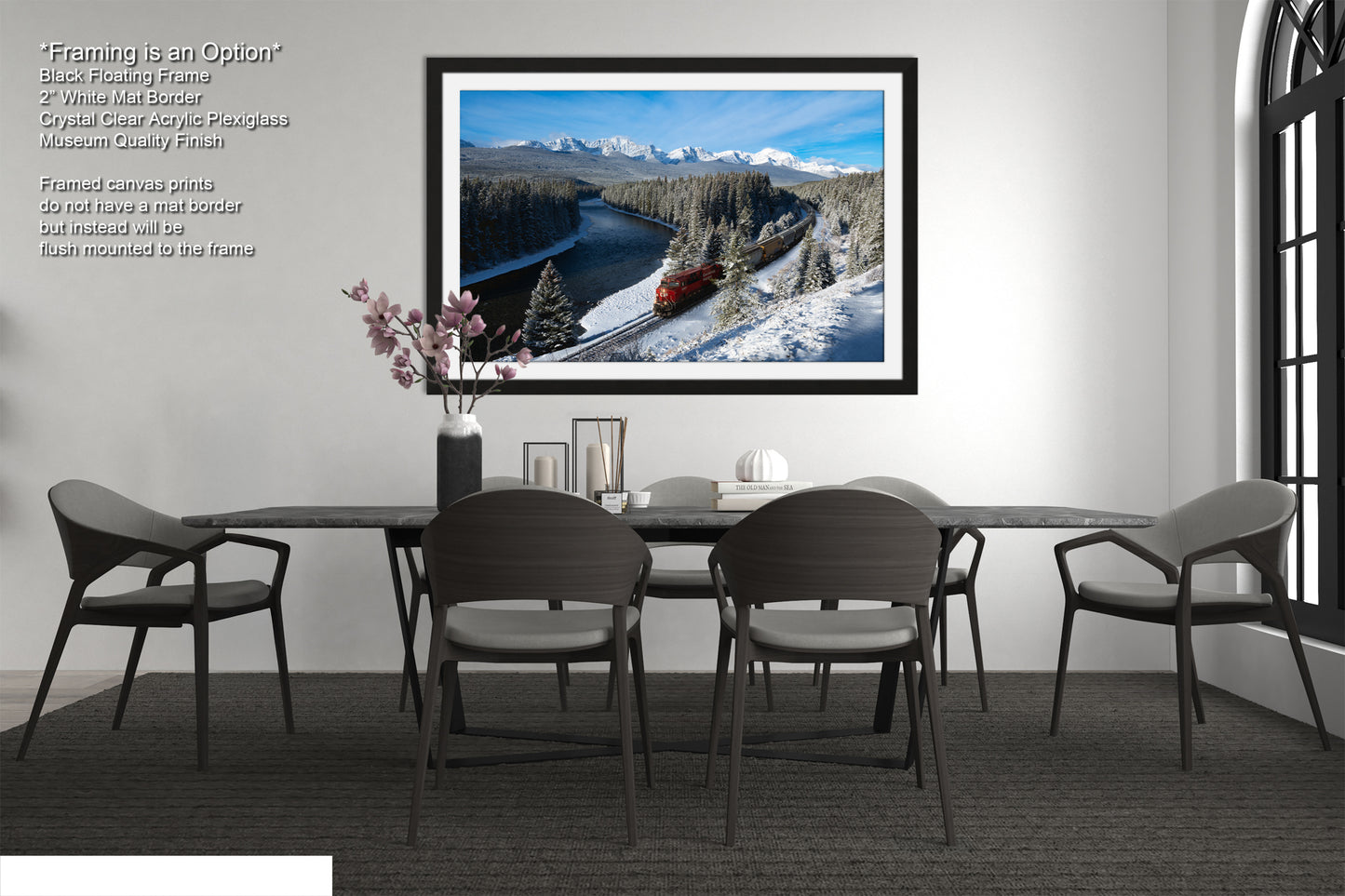 a modern dining room with a large black dining table surrounded by six chairs. Above the table, there is a framed picture of a snowy mountain landscape with a train passing through it. The room has a minimalist and clean design, with a white wall and a window providing natural light.