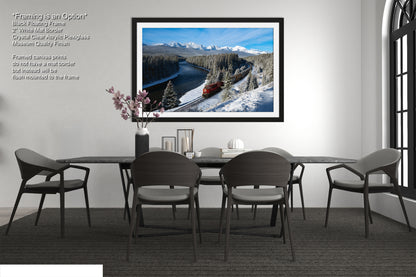 a modern dining room with a large black dining table surrounded by six chairs. Above the table, there is a framed picture of a snowy mountain landscape with a train passing through it. The room has a minimalist and clean design, with a white wall and a window providing natural light.