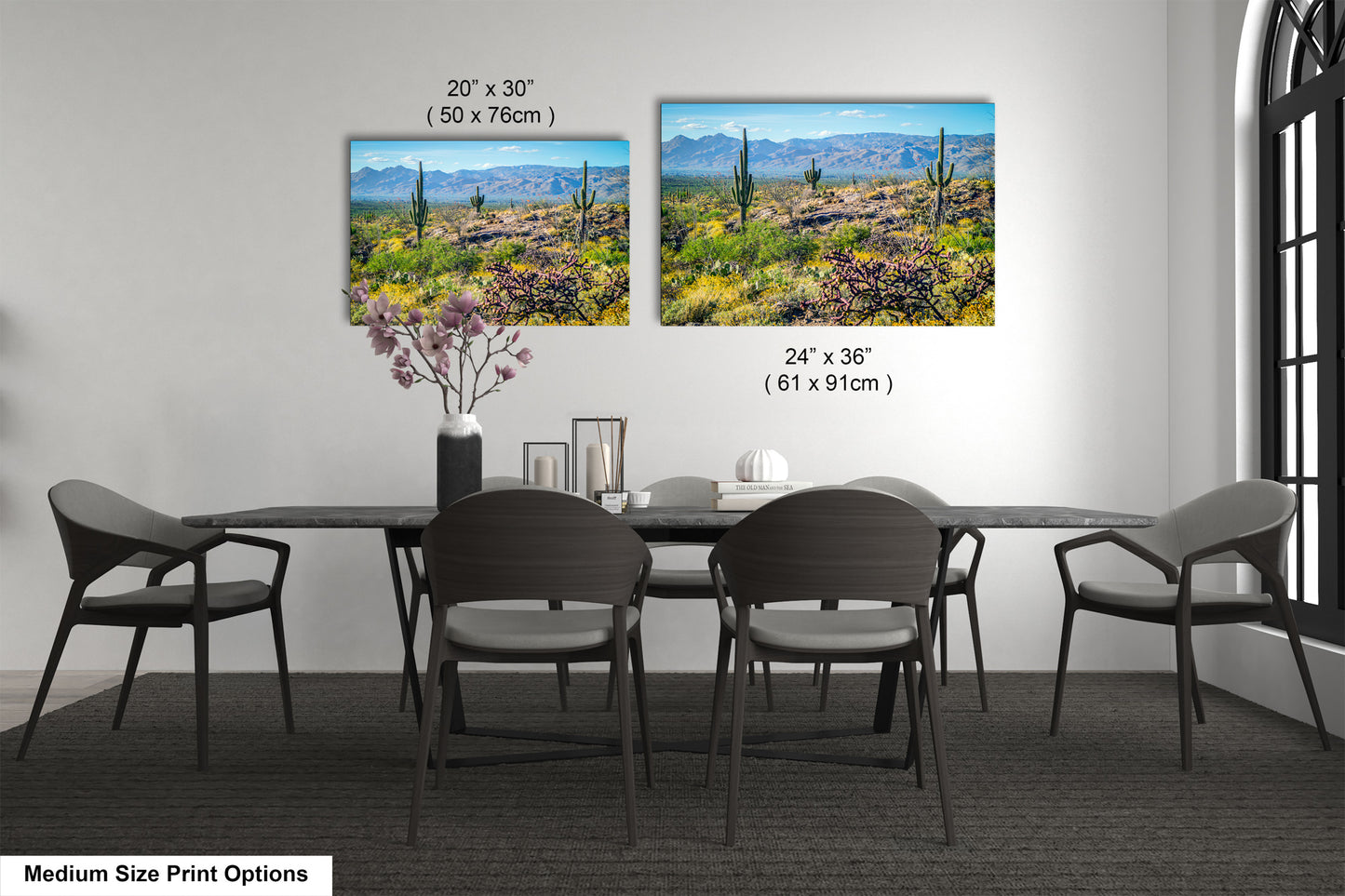 a modern dining room with a large black table surrounded by six chairs. Above the table, there are two framed prints of a desert landscape, providing a scenic view for the dining area. The prints are of different sizes, with one being 24x36 inches and the other being 24x30 inches. The prints are displayed on the wall, adding a touch of nature and artistry to the room.